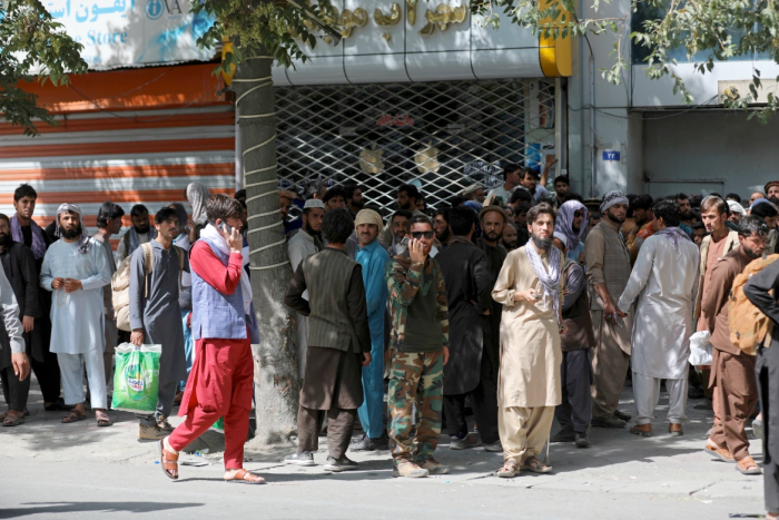 افغان ها ساعت ها در صف های طولانی منتظر می مانند تا پول را در مقابل یک بانک در کابل برداشت کنند. [Rahmat Gul/AP Photo]