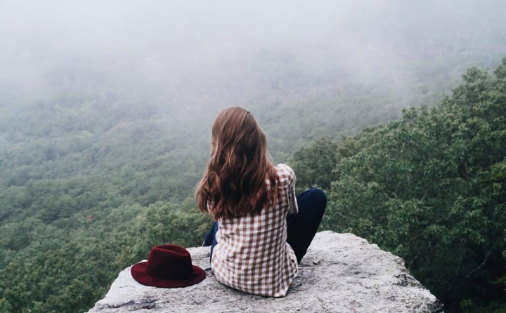 فواید تنهایی - زنی نشسته بر صخرهای با نمای جنگل