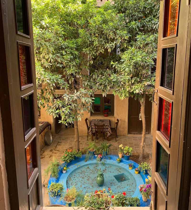 حوض فیروزه‌ای با گلدان های زیبا ازنمای پنجره خانه پرهامی شیراز