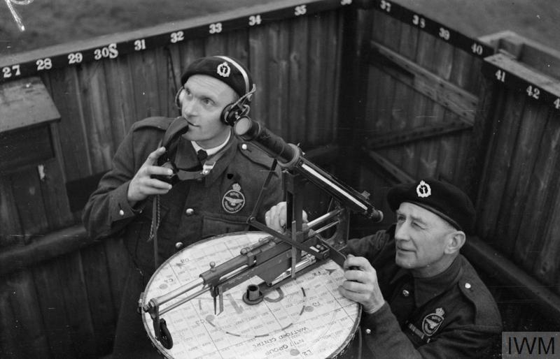 Using a chest telephone, Mr P C "Lofty" Austin, former commercial traveller and ex-professional footballer for Tottenham Hotspur, reports to the Corps Centre, as Mr E C "Smudge" Smith works the plotting instrument in an ROC post at Kings Langley, Hertfordshire.