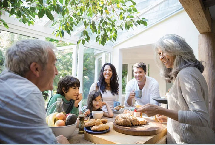 یک خانواده شاد شامل پدربزرگ و مادربزرگ، پدر و مادر و بچه‌ها دور میز صبحانه