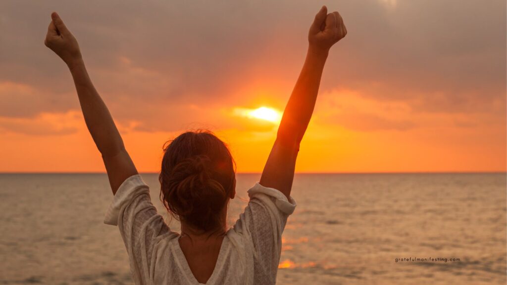 بلند کردن دست های زن در آسمان در حال غروب روبروی دریا