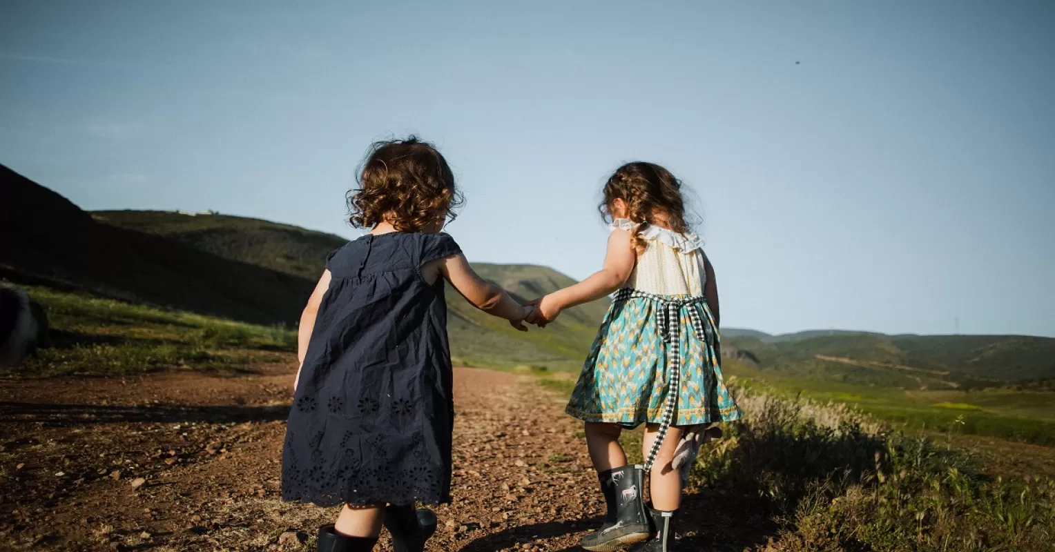 دو کودک دست در دست در حال راه رفتن در علفزار